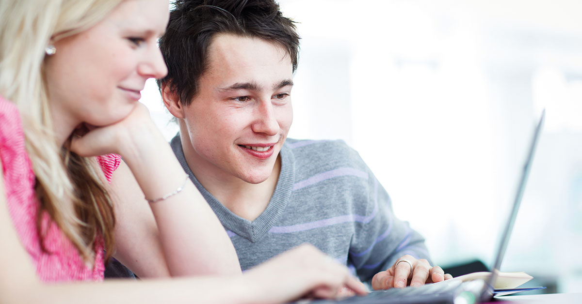 Two college students having fun studying together, using a lapto
